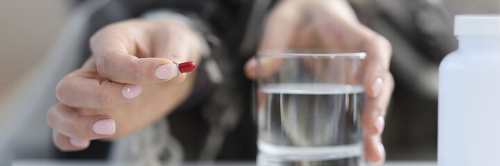 Female hands hold pill and glass of water.