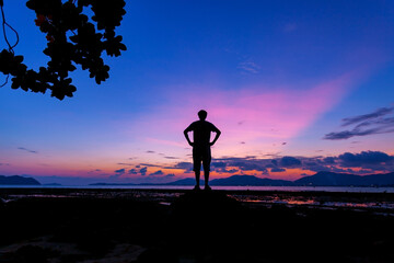 Obraz premium Silhouette of a man with Amazing Beautiful Light of nature Dramatic sky seascape in sunset or sunrise scenery background with leaves frame in the foreground.