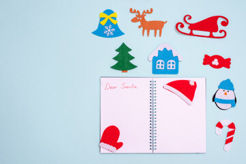 Flat composition with blank open notebook with inscription DEAR SANTA and christmas toys on blue background