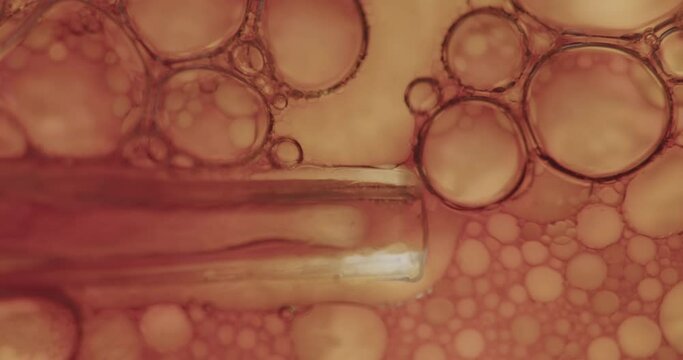 Small syringe entering cell structure, and dropping some new cells. Macro shot of air bubbles in transparent viscous liquid.
