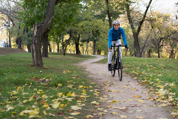 Fototapeta premium Young sporty man rides a bicycle through the park on a bicycle road. He has a safety helmet and jacket.