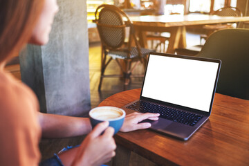 Mockup image of a woman touching on laptop computer touchpad with blank white desktop screen while drinking coffee