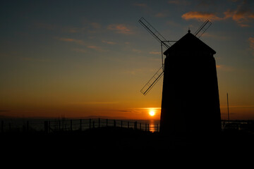 A view of sunset at St Monans, Fife,Scotland with a silhouette of the windmill and sun flare.
