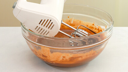 Chocolate cake batter in a glass bowl, and an electric mixer close up