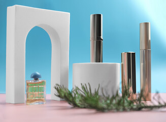 set of cosmetics on pink and blue background with white podium display and christmas tree branch. gift for woman. shiny mascara, lipsticks and perfum near trendy arch 