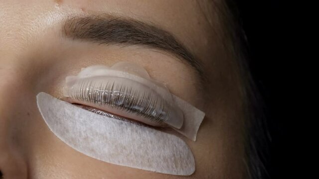 Face of a young girl before a modern eyelash lamination procedure in a professional beauty salon. The master applies a chemical during the eyelash curling procedure with a special brush close up.