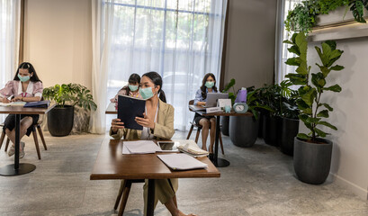Business in new normal. Office workers wearing face masks keep social distancing in an office to...