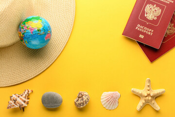 Tourist theme: Russian passport, hat, globe, seashells, starfish, and rock on a yellow background. Travel accessories. The globe shows Eurasia, China, India.