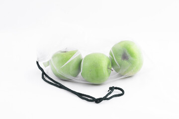 Three fresh sour healthy green apples on a white background are in an eco-friendly reusable bag-grid from the supermarket