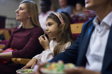 Fototapeta premium Family with child eating popcorn and watching a movie in the cinema