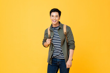 Portrait of smiling young male Asian tourist carrying backpack ready to travel in isolated studio...