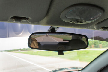espejo retrovisor dentro del auto por el cual se ve la carretera. también se ve pasto y día soleado.