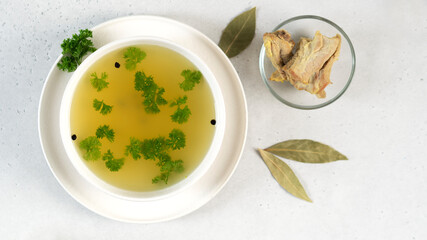Homemade turkey bone broth in white bowl with bay leaves, parsley and peppercorns. Health benefits. Collagen is good for joints.