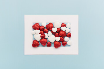 Valentine's Day holiday card. Red white small shiny hearts and white frame on pastel blue background. Valentines day concept.