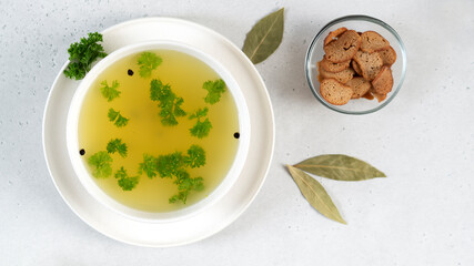 Homemade turkey bone broth in white bowl with bay leaves, parsley, peppercorns and croutons. Health benefits. Collagen is good for joints.