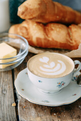 Cappuccino coffee on a wooden table with a loaf of bread. Breakfast with a buttered bun and a Cup of coffee.