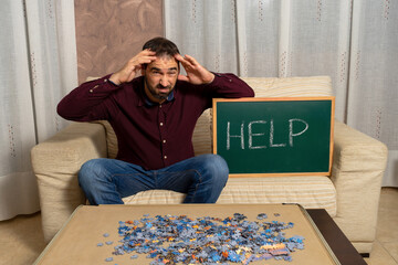 Young man with beard sitting on the couch at home doing puzzle
