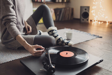Young woman listening to music, relaxing, enjoying life at home. Girl wearing warm winter clothes having fun. Turntable playing vinyl LP record. Leisure, music, hobby, lockdown, lyfestyle concept