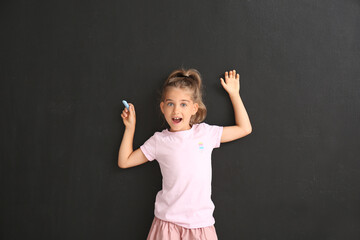 Cute little girl with chalk near black wall