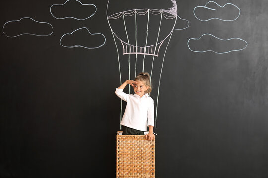 Cute little girl near black wall with drawn hot air balloon