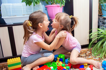 Two girls sisters play at home in a colored plastic construction set, argue about something and fight