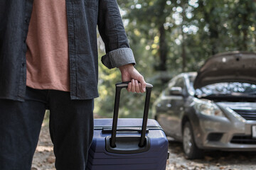 Obraz premium Man' hand drag to travel bag in front of open hood of a broken car on the road in the forest. Car breakdown concept.