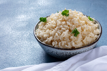 A bowl of white rice on a blue background, garnished with fresh parsley leaves