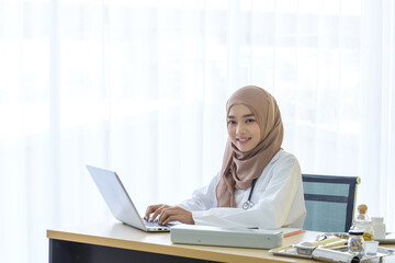 Young asian woman muslim doctor smile and looking at camera while working with laptop computer at hospital, Medicine and health care concept.