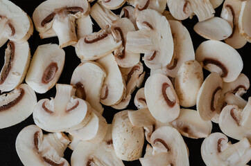 Group of raw champignons cut into pieces on black background.