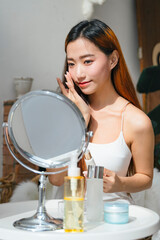 Beautiful asian woman using cosmetic for facial make up looking at mirror.