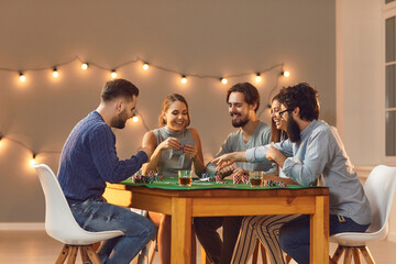 Happy young friends enjoying start of weekend, having drinks and playing game of poker