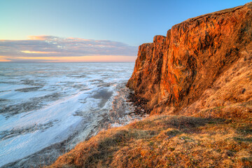 Picturesque arctic landscape. View from the coast to the cape and the frozen sea covered with ice. Beautiful rocks and cliff at sunrise. June in the Arctic. Cape Dionysius, Chukotka, Far East Russia.