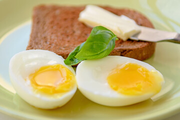 Two soft-boiled egg halves on a plate. Basil leaf, toast and butter. Close up.