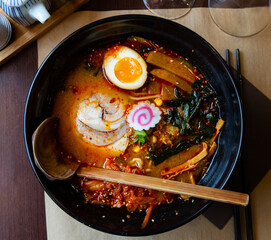 Traditional Japanese thick ramen served in black bowl with wooden spoon.