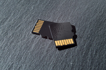 two micro sd cards lie on top of each other on a dark textured background, with golden contacts at...