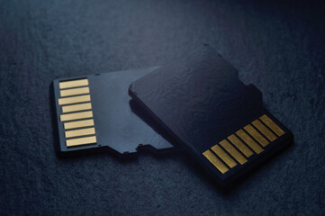 two micro sd cards lie on top of each other on a dark textured background, with golden contacts at...