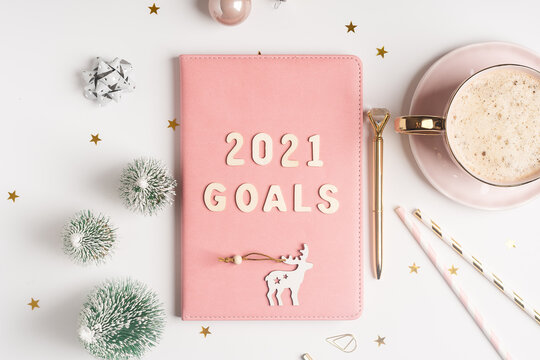 Desktop Christmas notepad with 2021goals letters text. Flat lay of white table background with planner, cup of coffee, Christmas decoration and stationery