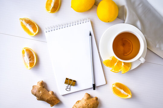 Trendy flat lay Ginger hot immunity boosting Vitamin natural drink With citrus lemon notebook and pencil on white background. Copy space