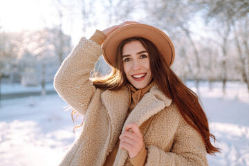 Stylish woman enjoying winter moments in a snowy park. Young woman in winter clothes posing with joy outside, frosty day. Youth, fashion, lifestyle and leisure concept.