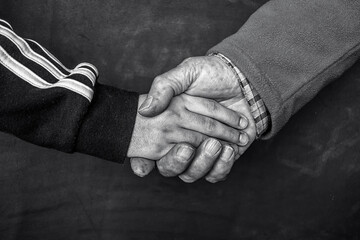 Two hands holding each other, one from a child and one from an old man. Black and white, selenium toning.