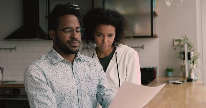 African married young couple holding papers read received correspondence letter document sit at apartment in kitchen, manage family finances, discuss money spend, expenses, get info about taxes refund