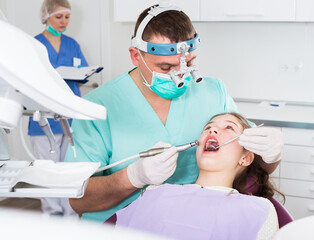Professional male dentist examining and performing treatment to teenage girl .