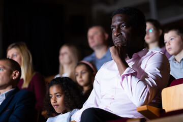 Portrait of interested african american theatergoer sitting in theater hall, watching theatrical...