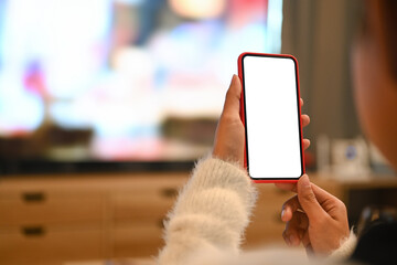 Cropped shot of young woman using blank screen mobile phone while sitting in living room.