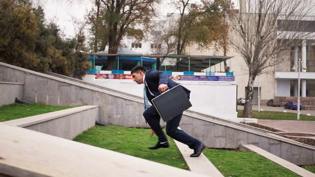 Young businessman in suit with black briefcase in his hands jumps up the parapets against city background. Business success teamwork concept. Career ladder concept. Corporate promotion. Slow motion.