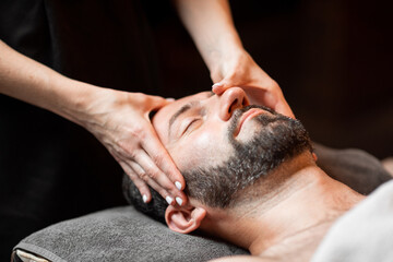 Obraz na płótnie Canvas Bearded man receiving a facial massage, relaxing at Spa salon, close-up