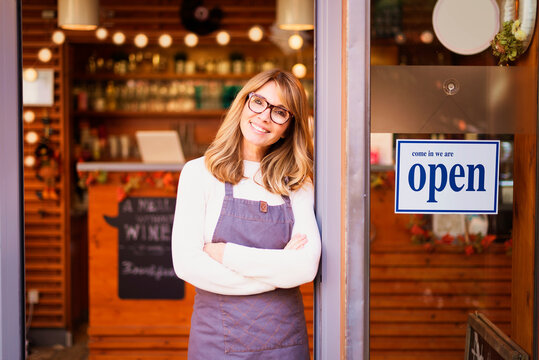 Smiling small business owner mature woman standing with arms crossed in the entrance of the cafe