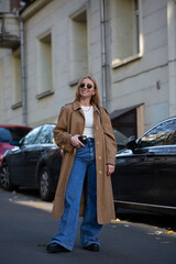 Obraz premium Young woman in a fashionable long coat walks in autumn city. copy space