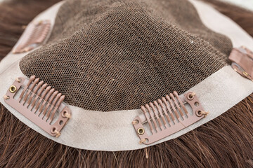 Closeup of the inside of a brunette toupee or wig. Wig clips attached on the side and mesh material.