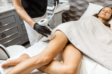 Fototapeta premium Young woman during an ultrasound liposuction procedure at luxury Spa salon. Doctor working on thigh area